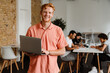 © Drobot Dean - Smiling man working on laptop computer while standing in office with his colleagues on a background