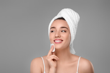 Wall Mural - Beautiful woman in terry towel removing makeup with cotton pad on gray background