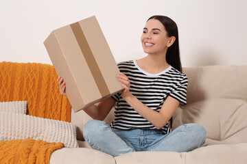 Wall Mural - Happy young woman with parcel on sofa at home. Internet shopping