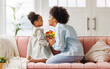© JenkoAtaman - Happy mother's day! Afro american family happy child daughter congratulates mom on holiday, hugs her and gives bouquet of flowers.