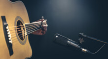 Male Musician Playing Acoustic Guitar Behind Microphone In Recording Studio.