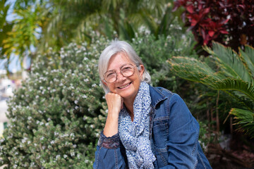 Sticker - Portrait of senior white-haired woman sitting in outdoor garden under the sun relaxing looking at camera smiling