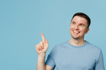 Wall Mural - Young smiling fun man wear casual t-shirt point index finger aside indicate on workspace area copy space mock up isolated on plain pastel light blue cyan background studio portrait Lifestyle concept