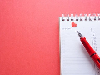 notepad with red heart and pen on a red workplace offiec background. blank notebook with text 