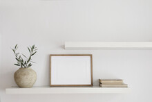 Elegant Interior Still Life. Two Floating Shelves. Blank Wooden Picture Frame Mockup Template. Textured Vase With Olive Tree Branches And Old Books. Modern Mediterranean Home. White Wall Background.