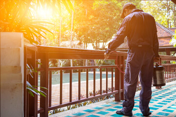 exterminate termite control company employee is using a termite sprayer at customer's house and searching for termite nests to eliminate. exterminate control worker spraying chemical insect repellant