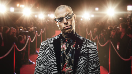 shot of tattooed rich guy dressed in trendy suit and glasses posing on red carpet.
