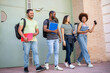 ©  Yistocking - A diverse group of college students. Happy casually dressed multiethnic young friends with textbooks and backpacks. The 4 young people leave through the door of the university. School break concept.