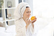 © sofiko14 - Serene healthy female after bath taking pleasure of fresh citrus fruit aroma while relaxing in peaceful bedroom interior. Charming adult person using rich in vitamin C orange for high-end beauty life.
