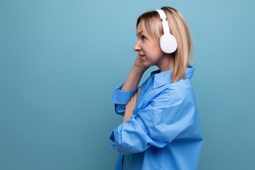 horizontal profile photo of an attentive young woman in a casual shirt focused on sound in large white headphones on a blue isolated background with copy space