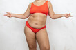 © Юля Бурмистрова - Naked overweight woman stand spreading arms to sides, white background. Woman in red underwear with cellulite hips and hanging large belly. Overeating, fat figure, plus size people, body positive.