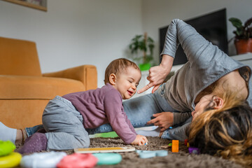 Wall Mural - One young woman a mother playing at home on the floor with her one year old child, family playtime, early child development concept