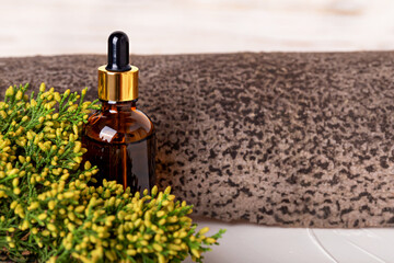 Glass cosmetic amber bottle with juniper branch near tree bark on white background close-up. Organic cosmetics. Lotion, tonic, gel, oil