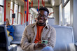 © Jovo Jovanovic/Stocksy - Smiling man listening music using mobile phone and earphones in tram
