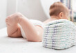 The legs of a baby in a diaper against the background of a stack of children's comfortable diapers, close-up