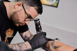 © Paula - Tattoo of a lion on the arm of the client in the salon. Tattoo artist working on a client's arm in his studio.