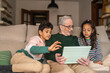 © Lupe Rodríguez/Stocksy - grandfather with his two grandchildren using ipad at home