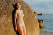 © Anna Tsukanova/Stocksy - Woman sunbathing leaning on huge boulder near the sea