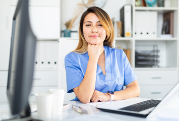 Woman doctor in uniform is working behind laptop in clinic