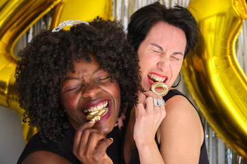 Two multiracial happy women in a 40 birthday party biting 40 birthday golden candles.