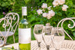 A wine bottle and wine glasses on a patio in a garden. Focus on the bottle.