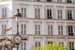 In Paris, France, a clock face on a street lamp in front of beautiful, traditional architecture in Montmartre.