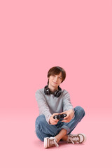 Wall Mural - Teenage boy with headphones playing video game on pink background