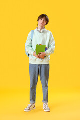 Canvas Print - Male student with copybooks and backpack on yellow background