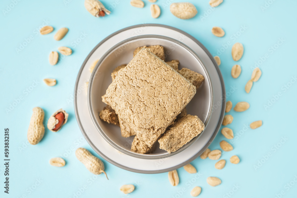 Bowl of tasty halva and peanuts on color background