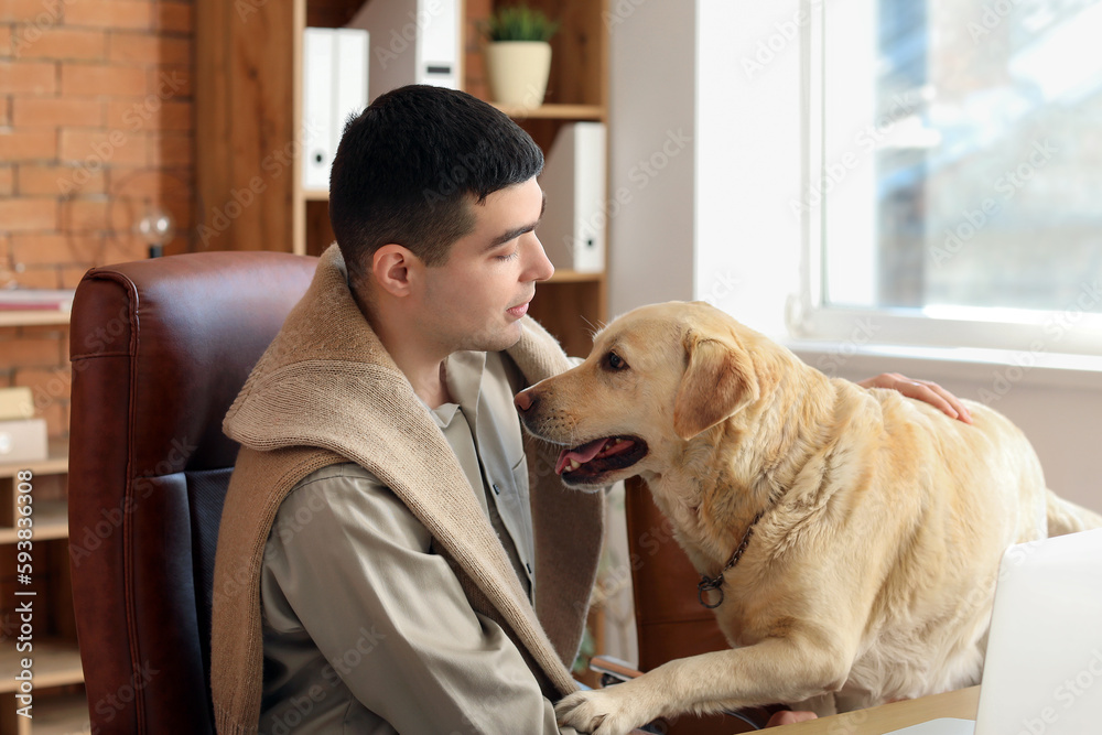 Young man with cute Labrador dog at table in office