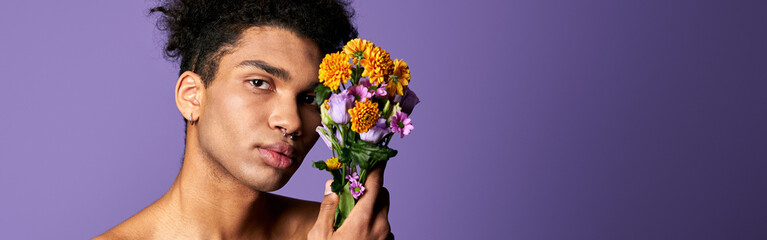 Wall Mural - Nacked hispanic male with flowers in hand posing on purple background. Transgender man nude torso