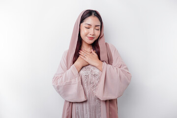 Happy mindful thankful young Asian Muslim woman with her hand on her chest smiling isolated on white background