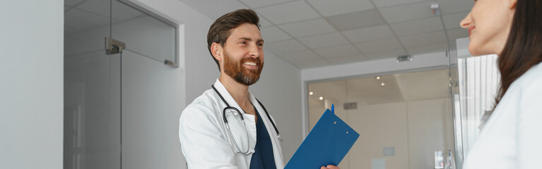 Wall Mural - Two doctors in uniform shaking hands standing in clinic hall near reception