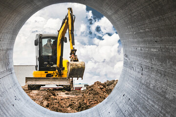 Wall Mural - Mini excavator at the construction site on the edge of a pit against a cloudy blue sky. Compact construction equipment for earthworks. An indispensable assistant for earthworks.