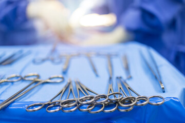 Wall Mural - A medical or surgical instrument for surgery inside the operating theatre with blur team of doctors in blue gown background.Surgical clamps for a surgeon on the blue tray.Blur background with light.