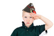 Young caucasian boy saluting playing dressups in green 'army' shirt and russian folding army hat - pilotka - from soviet red army with pins, badges recreated from original surplus from vintage Russia