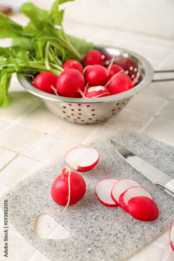 Board with fresh cut radish on light tile background