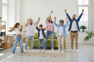 Happy extended multigenerational family all together having fun at home. Funny, overjoyed, excited mother, father, grandmother, grandfather and children dancing in a big, spacious living room interior