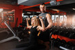 Exercises with dumbbells. Young girl does exercises lifting dumbbells. Young trainer helps to perform training.