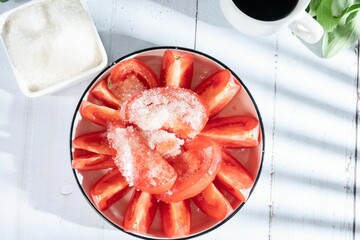 Sticker - Top view of neatly arranged tomato slices covered in salt in a round bowl beside a coffee cup