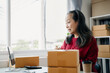 © NINENII - adult woman start up small business owner writing address on cardboard box at workplace.small business entrepreneur SME or freelance, female working with box at home.