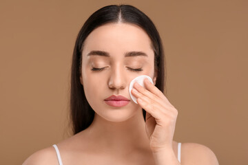 Wall Mural - Beautiful woman removing makeup with cotton pad on beige background