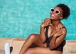 © Meeko Media - Beautiful Black woman applies sunscreen sitting by pool in summer sun
