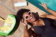 © Meeko Media - Overhead shot of young Black woman lying next to pool with purse, sunscreen