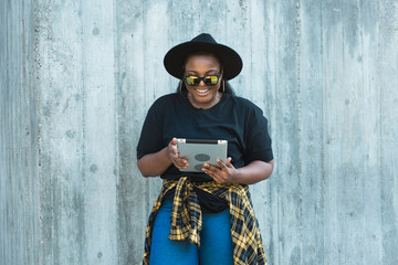 Portrait of beautiful curly African American girl standing urban background and holding digital tablet. charming young female with a tablet pc