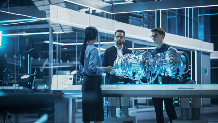 Fototapete - Young Team of Engineers, Project Manager and Machinery Operators Collaborate on a New Type of a Gas Turbine Engine, Standing with Tablet and Laptop Computers in Scientific Technology Lab. High Angle.
