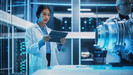 Fototapete - Middle Aged Engineer and Young Asian Scientist Collaborate on a New Type of Electric Turbine Engine, Standing and Using a Tablet Computers in Scientific Technology Laboratory.