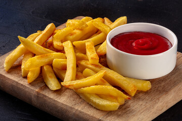 Poster - French fries, potato snack with ketchup, fast food on a dark stone background, a side dish on a wooden board