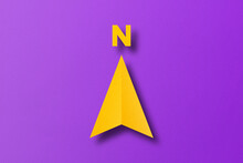 Yellow Paper Cut In North Arrow Shape Set On Purple Paper Background.
