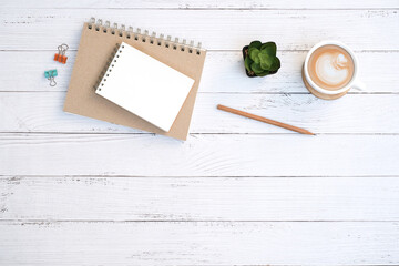 Wall Mural - Blank notepad and coffee cup with green plant on wooden white table desk background ,Top view with copy space, Flat lay  